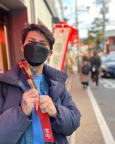 Artist Tenya Rodriguez wears a mask while holding red sticks.