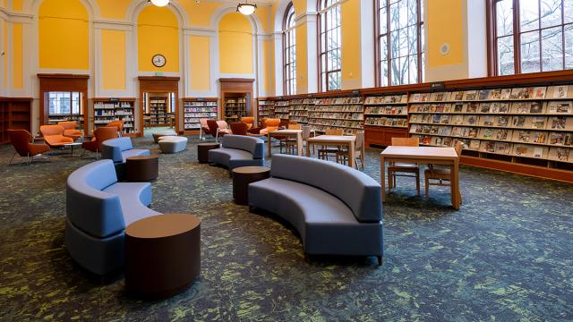 Soft blue seats are centered in a yellow room with bookshelves lining the walls