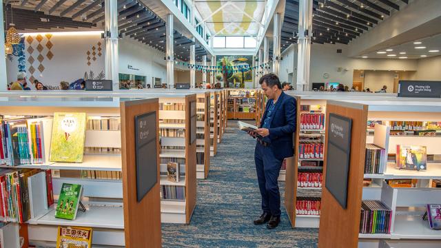 A man leans against bookshelves reading a book in Midland Library.