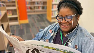 Black staff member smiling and reading an open newspaper