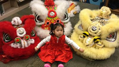 Child at Lunar New Year celebration sitting with three large lion masks