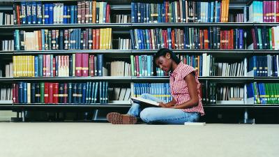 Una persona joven sentada en la biblioteca leyendo un libro