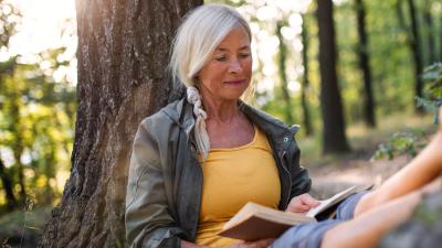 Older woman sitting in the forest reading a book