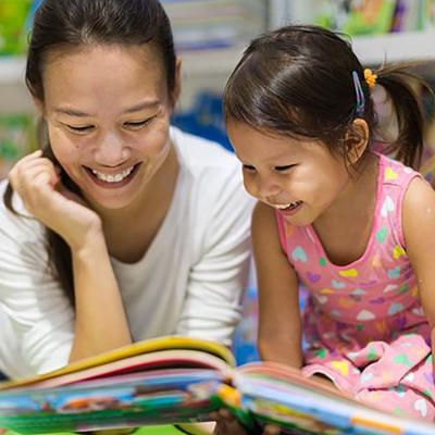 Smiling adult and child reading a kids' book together.