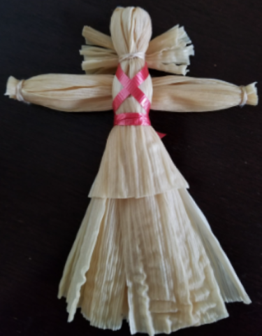 Photograph of a cornhusk doll with a pink ribbon tied around the bodice