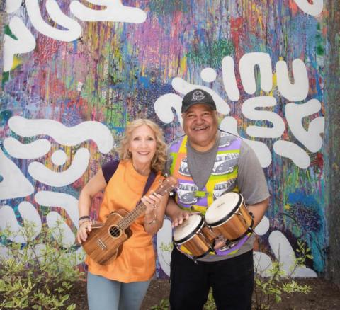 two smiling musicians holding instruments in front of a colorful wall