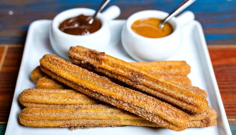 cinnamon and sugar covered churros on a plate in front of chocolate and caramel dipping sauces