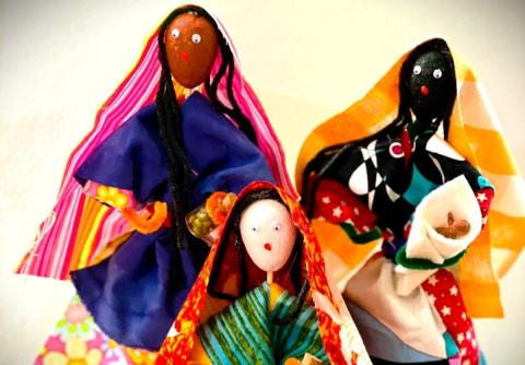 three traditional cloth dolls of different skin hues wearing colorful dresses
