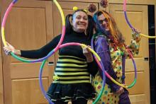 A photograph of two people in clownish costumes posing with four multicolored hula hoops