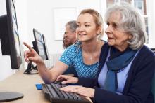 Photo of an younger woman helping senior woman on computer
