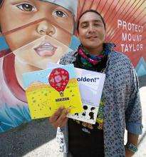 author Daniel Vandever holds his books Herizon and Fall in Line, Holden against the backdrop of a mural showing a child's face and the words 