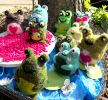 multiple stuffed felt frogs clustered at the base of a tree