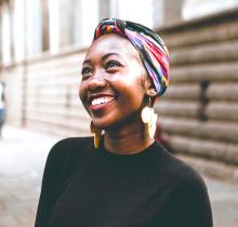 photo of a woman wearing a head wrap and earrings shaped like the African continent