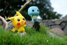Photo of two Pokemon figurines (Pikachu and Squirtle) standing outside in grass.