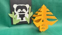 Photo of a yellow paper craft and a black paper with green and white cut designs.