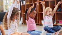 3 children seated with arms raised in a stretch