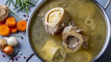 Stockpot with broth, bones, and various vegetables and herbs in the background