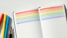Image of an open notebook highlighted in rainbow colors with markers and an ink pen resting next to it.