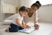 Photo of a black woman with a toddler, reading on the ground together