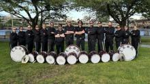 Photo of 15 people in black uniform with drums in a park