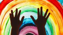 Photo of a child's hands above a rainbow painted on glass