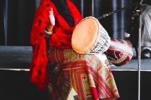 a photograph of a woman wearing Somali clothing, sitting playing a drum at a microphone