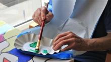 Photo of a senior citizen dabbing a paintbrush into green acrylic paint