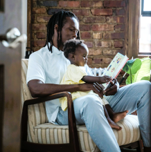 Photo of a Black person reading a story to a child in their lap