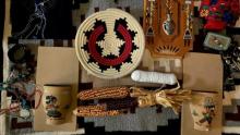 Photo of various items such as dried corn, woven materials, and turquoise beading laid on a patterned blanket.