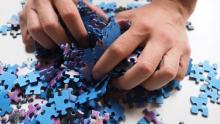 Photo of a person's hands mixing up a pile of blue and purple puzzle pieces