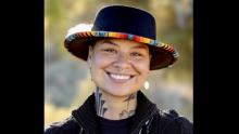 Photo of Shuína Skó in a colorfully embroidered hat, smiling