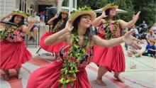 Photograph of four women dancing in red dresses with leaved garlands