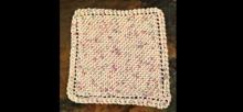 Photo of a cream knitted dishcloth with flecks of blue and purple.