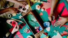 Photo of three people's hands crafting paper flowers at a table