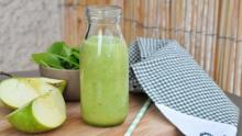 Photo of a green smoothie on a table beside a green apple and a black and white hand towel.
