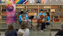 Photo of four performers from the Chamber Music Northwest Young Artist Institute performing with various string instruments at a library.