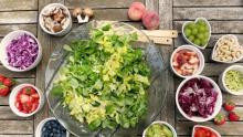Photo of a bowl of lettuce with a variety of ingredients around it to make a salad.