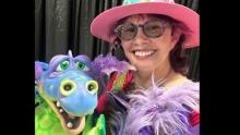 Photo of Ventriloquist Vikki in a pink hat with a green and blue dragon puppet