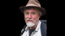 Photo of William Sullivan in a tan hat and outdoorsy clothes against a black background