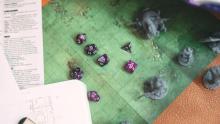 Photo of several purple dice and figures on top of a roleplaying map