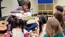 Photo of a woman reading a picture book to children, with guitar