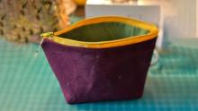 Photo of a purple unzipped pouch with a yellow zipper and green lining, sitting open on a fabric cutting mat.