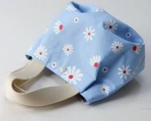 Photo of a blue tote bag with white flower pattern and white handles on a white background.