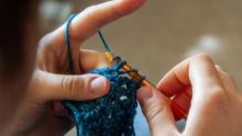 Photo of a person crocheting with blue yarn.