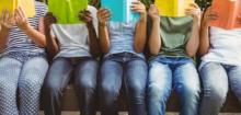 Five children sitting in a row, each reading a book held up in front of their faces