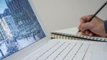Photo of a person writing on a notepad next to a laptop.