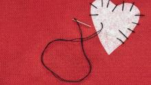 Red fabric background with a white fabric heart stitched on top with black thread and needle.