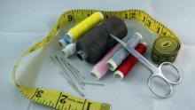 Photo of several colors of sewing thread, needles and a pair of scissors surrounded by a loop of yellow measuring tape.