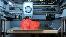 Photo of a Bambu printer working on a red project.