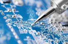 Image of a blue micro circuit board being soldered by the tip of a silver soldering iron.